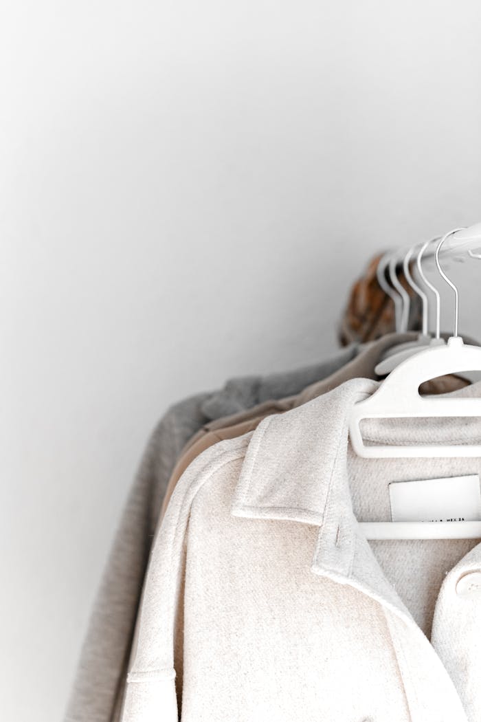 A selection of neutral-colored clothes hang neatly on white hangers against a plain backdrop.