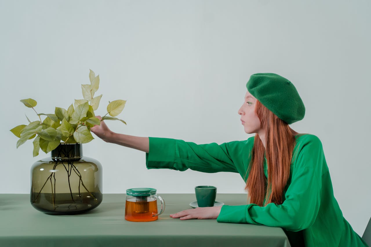Side view of woman in green beret arranging leaves in glass vase.